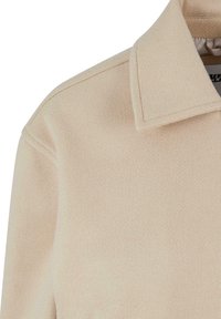 Beige ullblandingsjakke med strukturert krage, myk tekstur og rene linjer. Detaljert søm er synlig langs sømmene.