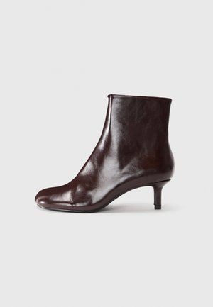 Brown leather ankle boot with a sleek design, pointed toe, and a thin, short heel. Smooth texture with minimal detailing.
