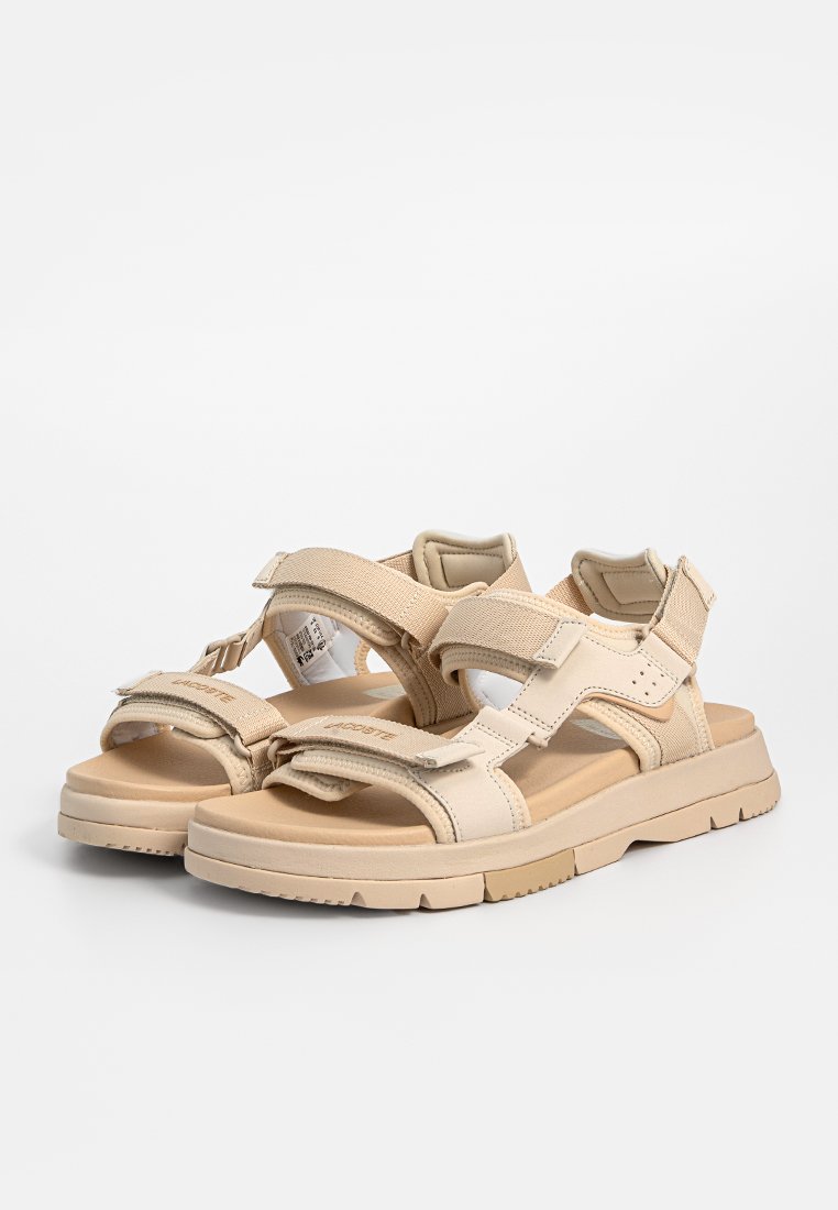 Sandales beige avec plusieurs sangles réglables en Velcro, une semelle intérieure rembourrée et une semelle en caoutchouc épaisse présentant des motifs texturés.