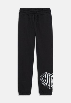 Pantalones deportivos negros fabricados en material suave, con un gráfico de logo en blanco en la pierna izquierda. Cintura elástica con cordón y puños ajustados.