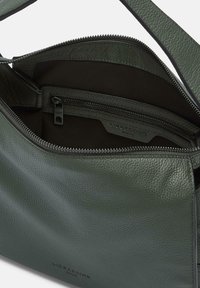 Zielona skórzana torba noszona na krzyż z teksturowanym wykończeniem, z zamykaną na zamek wewnętrzną kieszenią i metką z logo w środku, prosty design i praktyczny układ.