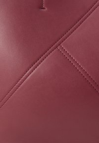 Bordo kožni ručni torba s glatkom teksturom, s dijagonalno ušivenim detaljima i minimalističkim dizajnom.