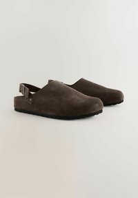 Braune Wildleder-Clogs mit offenem Rücken, mit einem geschwungenen Design, verstellbarem Riemen und strukturiertem schwarzen Gummisohle.