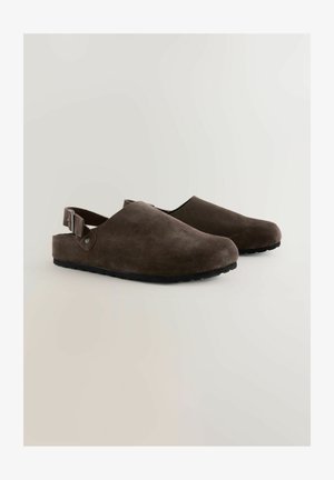 Rudi suede klumpiai su atvira nugara, turintys kreivinę formą, reguliuojamą diržą ir tekstūruotą juodą guminį padą.