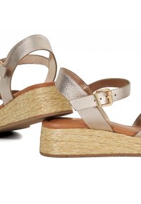 Wedge sandalen met metallic gouden faux leren banden, verstelbare gesp en een natuurlijke geweven jute hak. Gladde binnenvoering en rubberen buitenzool.