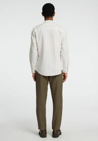Camisa de manga larga a rayas en colores claros. Corte holgado, dobladillo redondeado, puños abotonados, combinada con pantalones tapered en verde oliva y zapatos marrones.