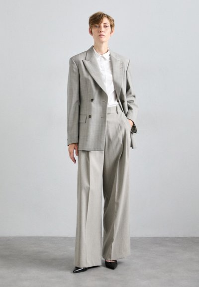 Light gray oversized double-breasted blazer with peak lapels, paired with wide-leg trousers. White collared shirt underneath. Black pointed shoes.