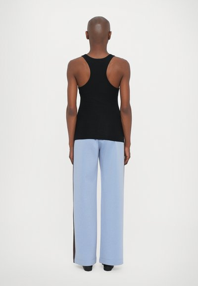 Top sin mangas negro de corte racerback combinado con pantalones anchos de tiro alto azul claros, que presentan un detalle de franja lateral. Textura suave, parte superior ajustada y parte inferior holgada.