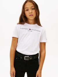 Λευκό βαμβακερό t-shirt με την ένδειξη "TOMMY HILFIGER EST. 1985" τυπωμένο σε ναυτικό και κόκκινο χρώμα. Συνδυάζεται με μαύρα τζιν παντελόνια και μαύρη ζώνη με ασημένιο κούμπωμα.