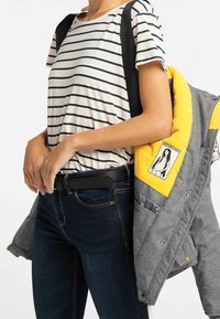 Randig kortärmad skjorta med svart och vita ränder, kombinerad med mörka jeans och en grå jacka med gul foder och patchdetalj.