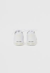 Bílé sportovní boty s vrchní částí z síťoviny, tkaničkami a výrazným designem paty, který zahrnuje průhlednou vzduchovou polstrovanou jednotku.