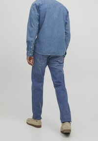 Camisa de mezclilla azul clara con cierres de botón, combinada con jeans azul claros. Calzado beige completa el conjunto. Textura suave, ajuste casual.