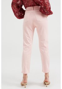 Vaaleanpunaiset farkut, joissa on istuva vyötärö, suorat lahkeet ja näkyvät takataskut, yhdistettynä kuviolliseen paitaan ja korkokenkiin.