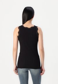Top negro sin mangas con detalles de encaje en los hombros, diseño ajustado y textura suave, combinado con jeans de mezclilla azul.