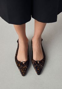 Ballerine con stampa leopardata, punte strette, talloni aperti e un dettaglio decorativo in argento sulla parte anteriore. Tessuto morbido e strutturato.