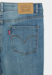 Jeans de denim azul con una etiqueta de cuero marrón con diseño en relieve. Bolsillo trasero con patrón de costura distintivo y detalle de etiqueta roja.