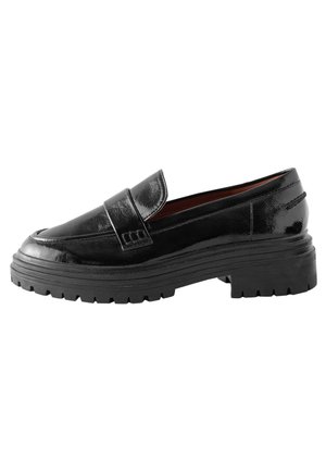 Mocassin en cuir noir brillant avec semelle épaisse crantée et petit talon, style à enfiler, coutures visibles et détail de sangle sur le dessus.