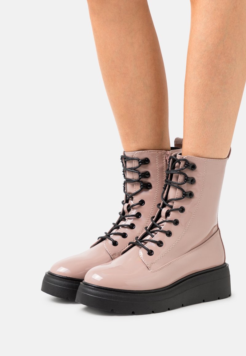 Bottines à lacets rose brillant avec des lacets noirs, une semelle plate et des détails de couture subtils. Texture lisse avec un design à bout arrondi.