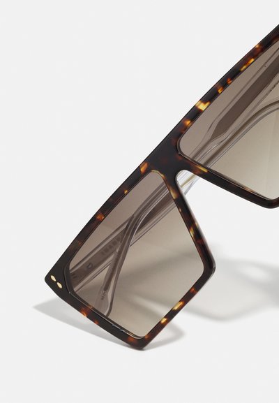 Schildpadkleurige zonnebril met schuine monturen, donkere glazen en transparante pootjes. Bevat twee gouden accenten op het montuur.