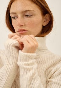 Sweter z golfem w kolorze kremowym, wykonany na drutach, z prążkowaną fakturą, długimi rękawami i luźnym krojem, charakteryzujący się przytulnym designem zbierającym się przy dekolcie.