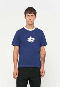 Marineblå bomulds t-shirt med hvid ribbet krave, prydet med et grafisk stjernetegn i hvidt med sort kant på brystet, korte ærmer.