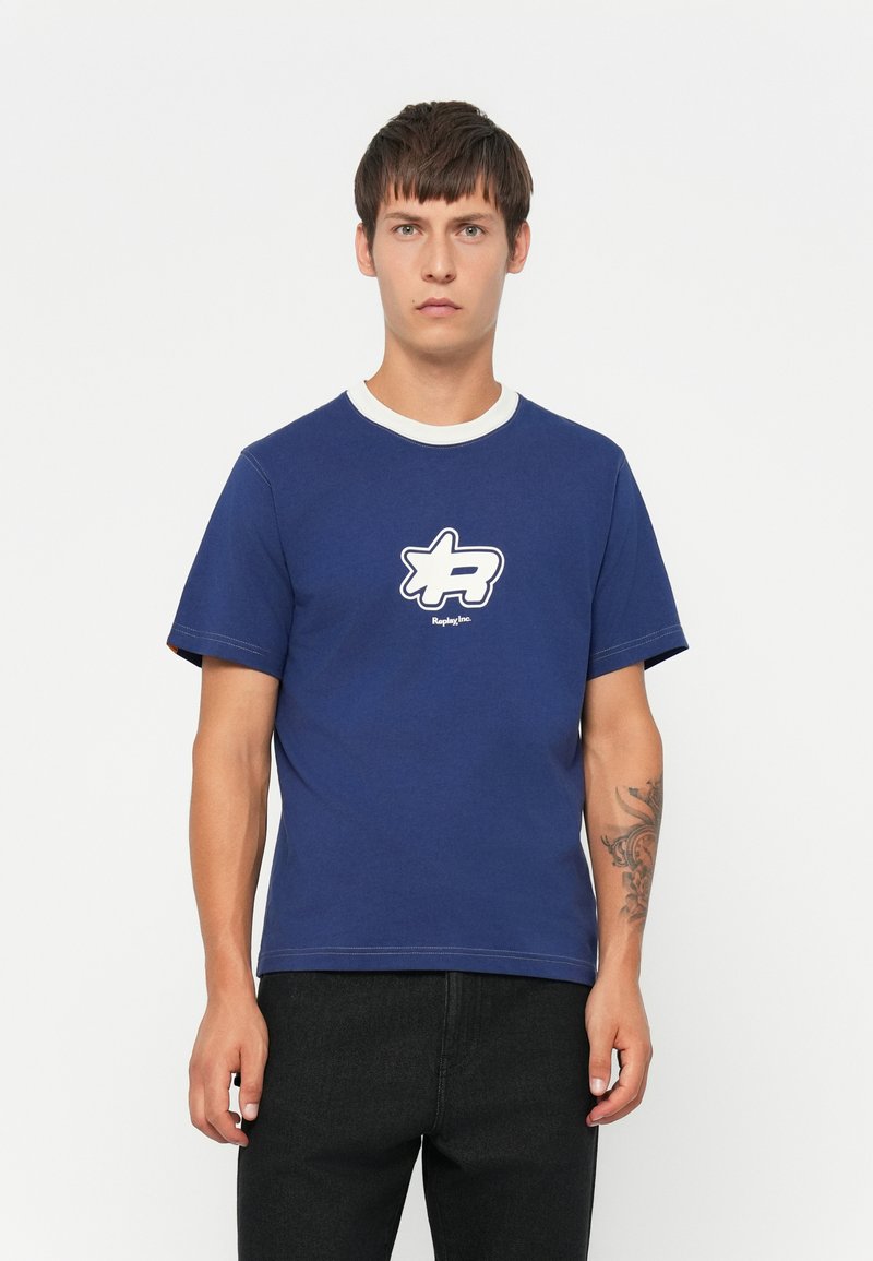 Marineblå bomulds t-shirt med hvid ribbet krave, prydet med et grafisk stjernetegn i hvidt med sort kant på brystet, korte ærmer.