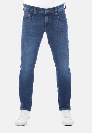 Jeans in denim blu con una vestibilità slim, cinque tasche, passanti per cintura e cuciture a contrasto, abbinati a sneakers bianche.