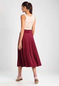 Débardeur beige à côtes avec des bords volants associé à une jupe midi plissée bordeaux, avec une large taille et un tissu doux et fluide.