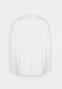 Chemise blanche à manches longues avec un col rond, une texture lisse, des fentes sur les côtés et des manches avec poignets. Design minimaliste sans logos visibles.