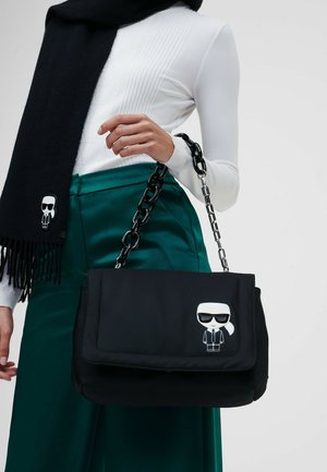 Black handbag with a soft texture, chain strap, and a graphic of a figure wearing sunglasses. Features a flap closure and a smooth surface.