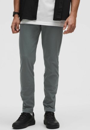 Pantalon gris slim en tissu léger, à la texture lisse et à la taille élastique, associé à des baskets noires.