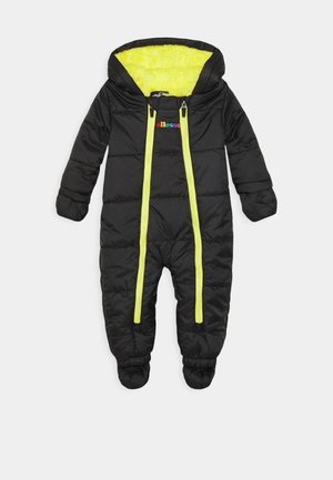 Combinaison de neige pour bébé noire avec moufles intégrées, double fermeture éclair jaune, doublure intérieure jaune vif et logo "ellesse" multicolore sur la poitrine.