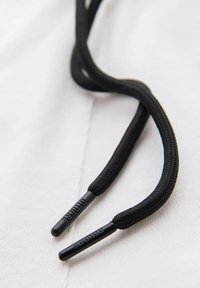 Gros plan de lacets noirs avec embouts en plastique, reposant sur un fond en tissu blanc.