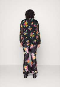 Sorte bluse med blomsterprint og lange ærmer, sat sammen med sorte bukser med farverige blomsterdetaljer. Glat stof, let og luftig design.