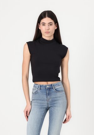 Black cropped sleeveless top with a high neck, made from a smooth fabric, paired with light blue high-waisted jeans. Simple design, fitted look.