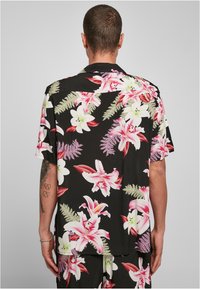Cămașă cu mânecă scurtă, de culoare neagră, cu un model floral vibrant în roz și alb, realizată dintr-un material fin și având o croială lejeră, ideală pentru purtarea de zi cu zi.