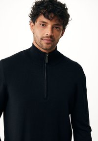 Pullover nero con zip alta, realizzato in un tessuto morbido. Il design include una zip a un quarto e dettagli a coste sul colletto.