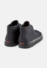 Black high-top shoes with a textured fabric upper, rubber sole, and Camper logo on the back. Laced design with a smooth finish.