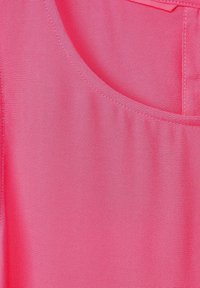 Ljust rosa tyg med en slät textur, rund halsringning och en liten fickdetalj på vänster sida.