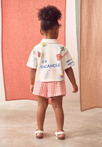 Short-sleeve, white shirt with colorful graphics and the text "EN VACANCES" on the back, paired with pink gingham shorts and white sandals.