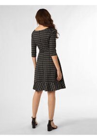 Schwarzes und graues Hahnentrittmuster-Kleid mit Dreiviertelärmeln, taillierter Taille und ausgestelltem Rock. Getragen mit schwarzen Riemchen-Absätzen.