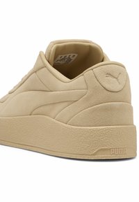Beige mocka sneakers med rund häl, texturerad sula och upphöjd logga på baksidan, med en sömlös design och vadderad krage.