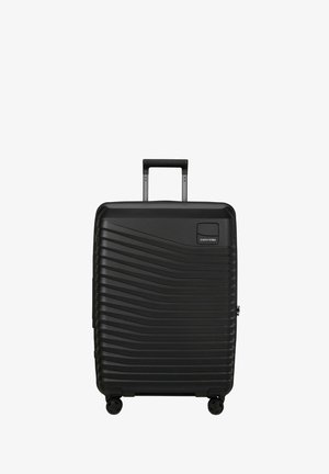 Valise rigide noire avec des rainures horizontales ondulées, poignée télescopique déployée, quatre roues multidirectionnelles et logo Samsonite à l'avant.