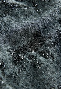 Texturovaná tmavě šedá látka s načechranými vlákny, zdobená rozptýlenými černými flitry, které vytvářejí třpytivý efekt.