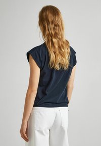 Tmavě modré bavlněné tričko s ohrnutými krátkými rukávy, volným střihem a kulatým lemem, doplněné bílými kalhotami s vysokým pasem.