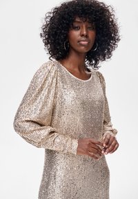 Długa sukienka z długim rękawem zdobiona złotymi cekinami, z okrągłym dekoltem, teksturowaną tkaniną oraz lekko bufionymi ramionami i luźnym krojem.