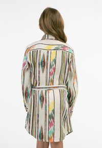 Abito camicia a fantasia in crema con righe verticali multicolori. Presenta un colletto, maniche lunghe e una cintura legata in vita.