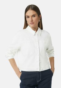 Witte denimjas met een puntige kraag, knoopsluiting, twee borstzakken en opgerolde mouwen, gecombineerd met donkerblauwe jeans.
