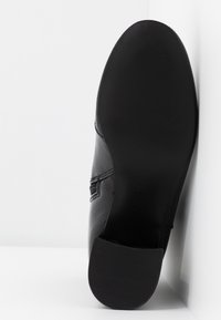 Semelle de chaussure habillée en cuir noir face à la caméra, montrant un motif lisse avec un talon bas et rectangulaire sur un fond blanc.