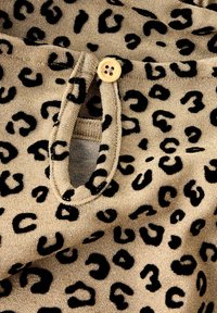 Bežna tkanina s črnim leopardskim vzorcem, ki ima mehak teksturo in gumbasto zapiranje. Oblikovanje vključuje majhno odprtino na pasu.